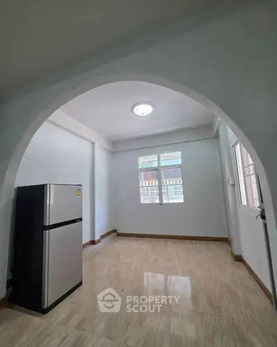 Spacious kitchen area with modern fridge and arched entryway, featuring bright natural light.