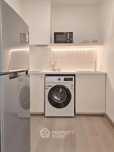 Modern kitchen with sleek appliances including fridge, washing machine, and microwave in a compact layout.