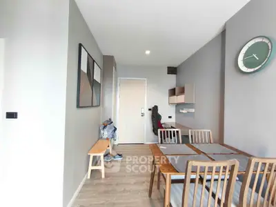 Modern dining area with wooden table and chairs, wall clock, and minimalist decor in a stylish apartment.