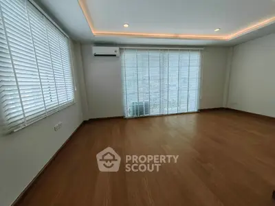 Spacious empty room with wooden flooring and large windows with blinds, perfect for customization.