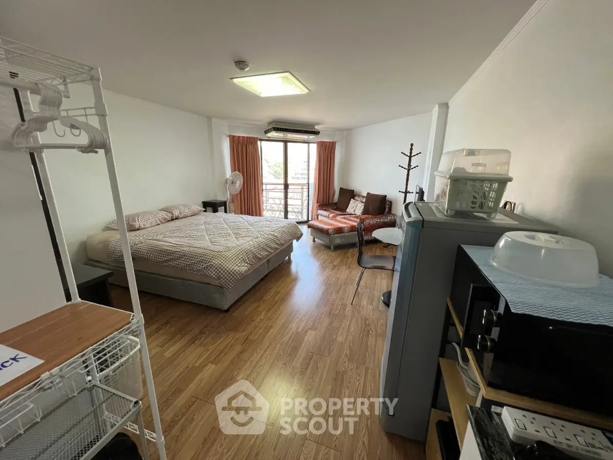 Spacious studio apartment with cozy bed and seating area, featuring wooden flooring and natural light.