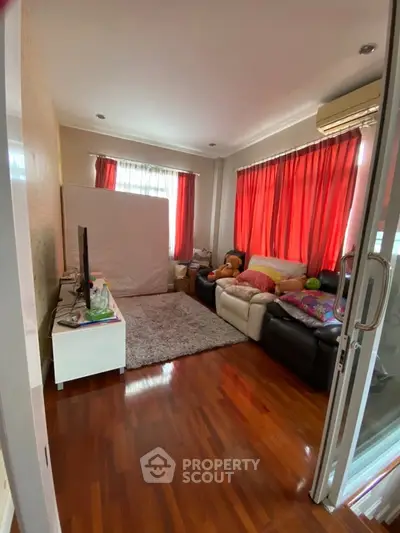 Cozy living room with wooden flooring, red curtains, and comfortable seating.