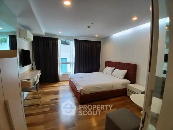 Spacious modern bedroom with wooden flooring and large window