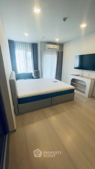 Spacious bedroom with modern decor, featuring a large bed, wall-mounted TV, and natural light from large windows.