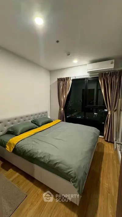 Modern bedroom with cozy bed and city view, featuring elegant curtains and wooden flooring.