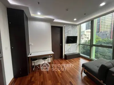 Modern living room with hardwood floors, large window, and wall-mounted TV in urban apartment.