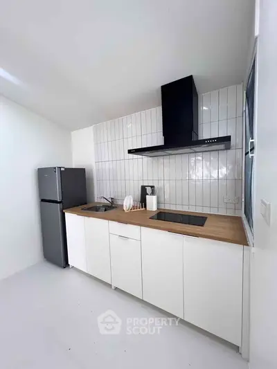 Modern kitchen with sleek white cabinets, wooden countertop, and stainless steel appliances.