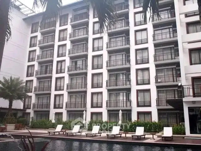 Luxurious apartment building with poolside lounge chairs and lush greenery.