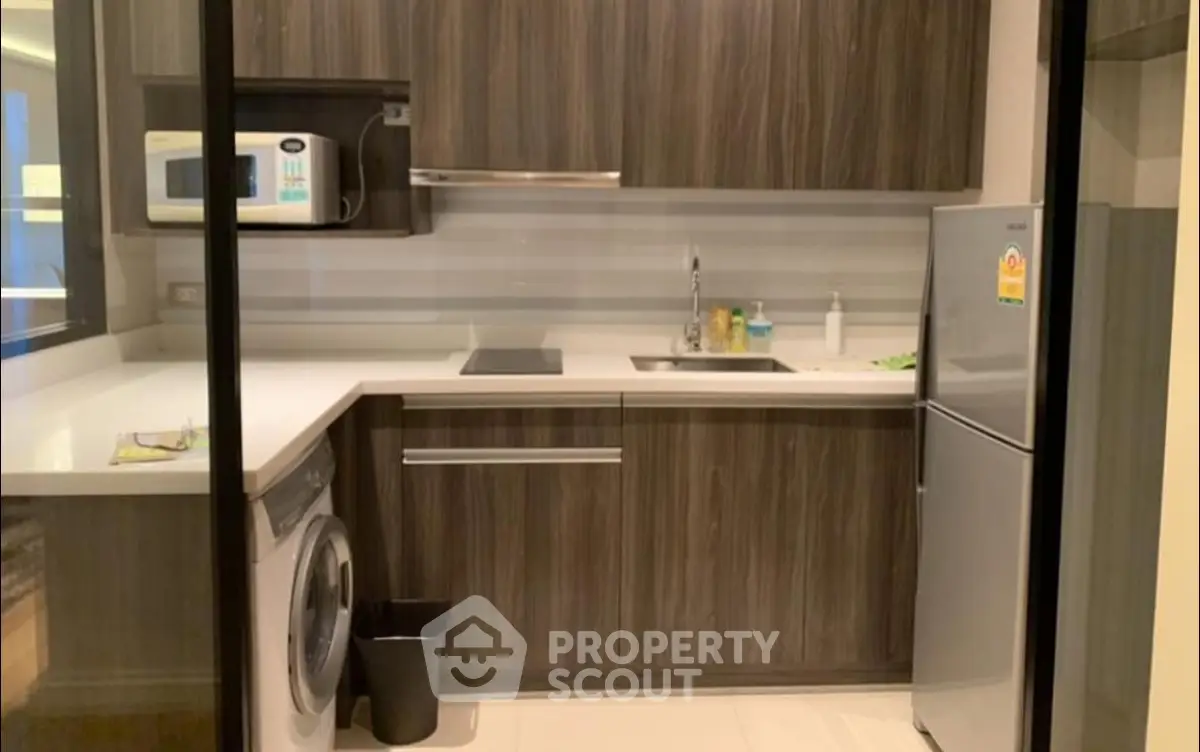 Modern kitchen with sleek cabinetry, washing machine, and compact fridge.