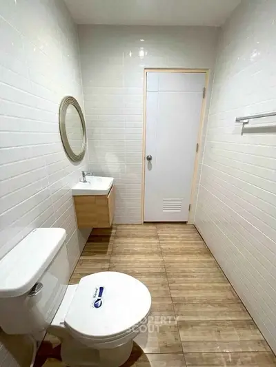 Modern bathroom with sleek fixtures and wooden flooring, featuring a round mirror and compact vanity.