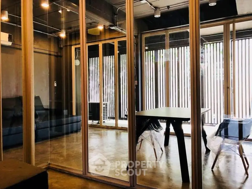 Modern industrial-style living room with glass partitions and sleek furniture.