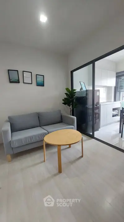 Modern living room with sleek sofa and round table, adjacent to a stylish kitchen.