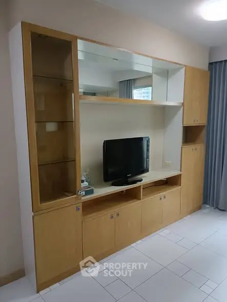 Spacious living room with modern wooden entertainment unit and sleek tile flooring.