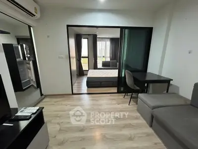 Modern apartment interior with open living room and bedroom, featuring sleek furniture and wooden flooring.