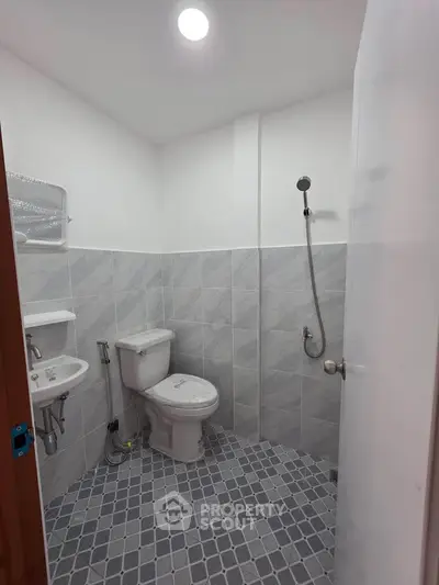 Modern bathroom with sleek tiles and compact design, featuring a toilet, sink, and shower area.