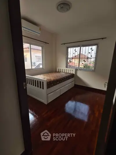 Cozy bedroom with wooden flooring and natural light from two windows.