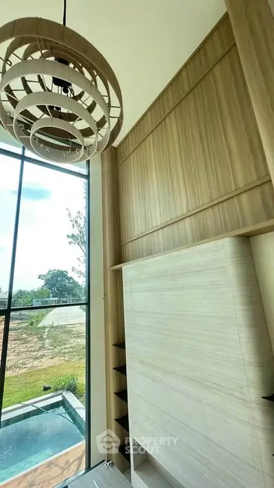Luxurious high-ceiling living room with modern chandelier and large windows overlooking a serene outdoor view.