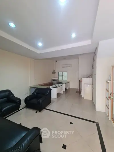 Spacious open-plan living room with modern kitchen and sleek black leather sofas.