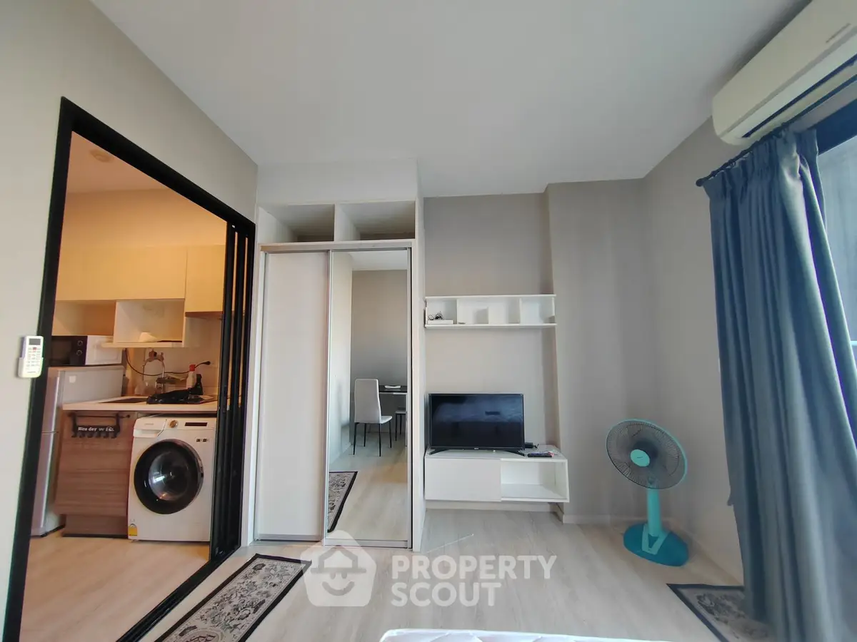 Modern living room with washing machine and TV, featuring sleek design and natural light.