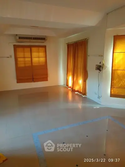 Spacious empty room with tiled flooring and warm natural light from large windows.