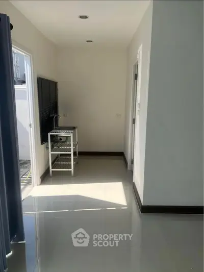 Bright hallway with glossy floor and small utility table, leading to outdoor area.