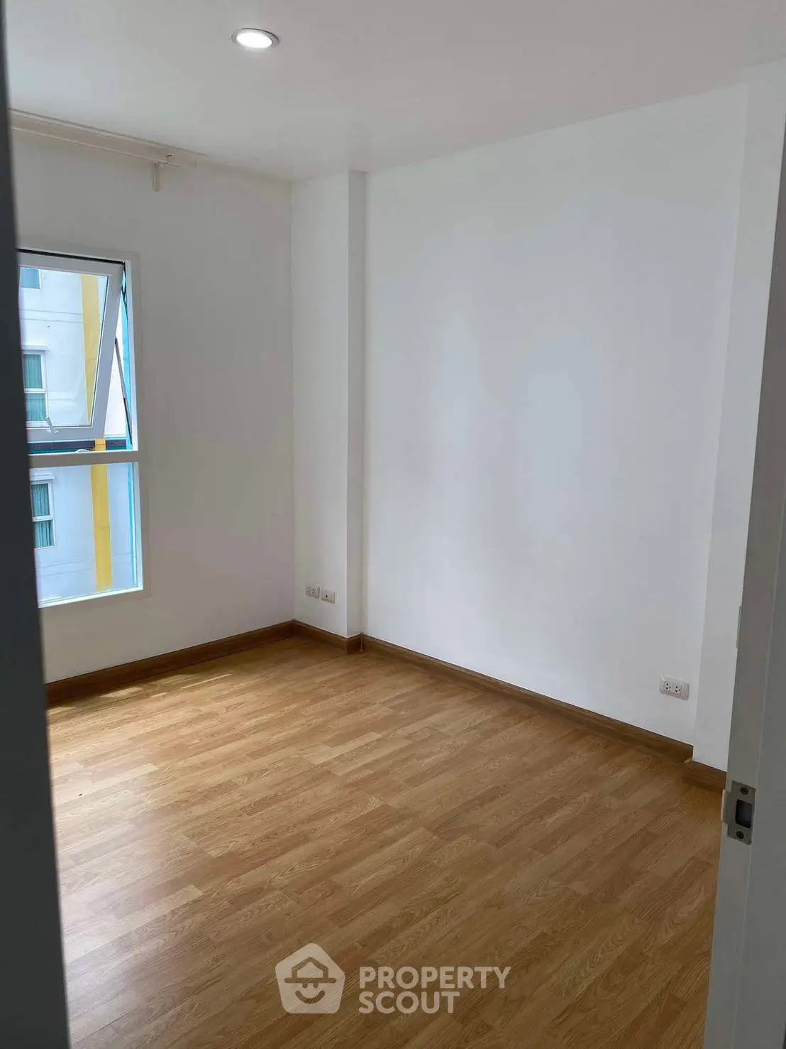 Spacious empty room with wooden flooring and large window in modern apartment.