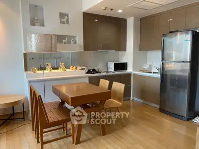 Modern kitchen with sleek cabinets, dining table, and stainless steel fridge in a cozy apartment.