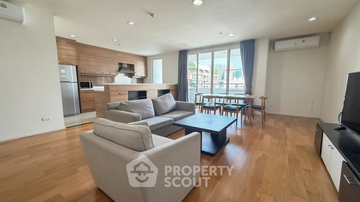 Spacious modern living room with open kitchen and city view, featuring wooden flooring and stylish furniture.