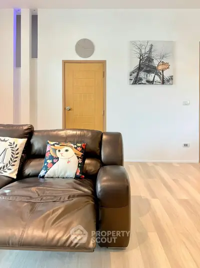 Modern living room with stylish leather sofa and decorative pillows, featuring minimalist decor and wooden flooring.