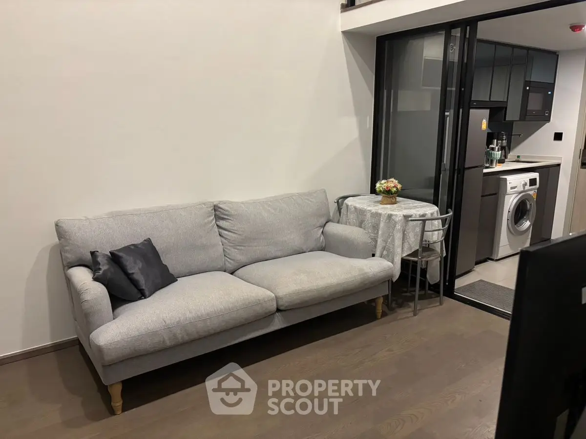 Modern living room with cozy sofa and open kitchen featuring washing machine