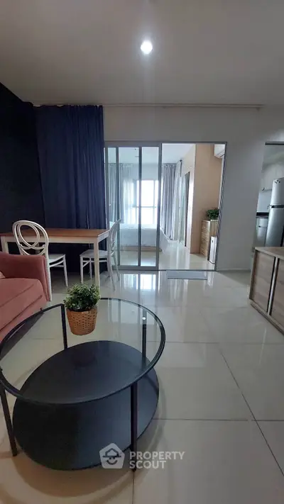 Modern open-plan living room with glass doors leading to a cozy bedroom, featuring stylish furniture and natural light.