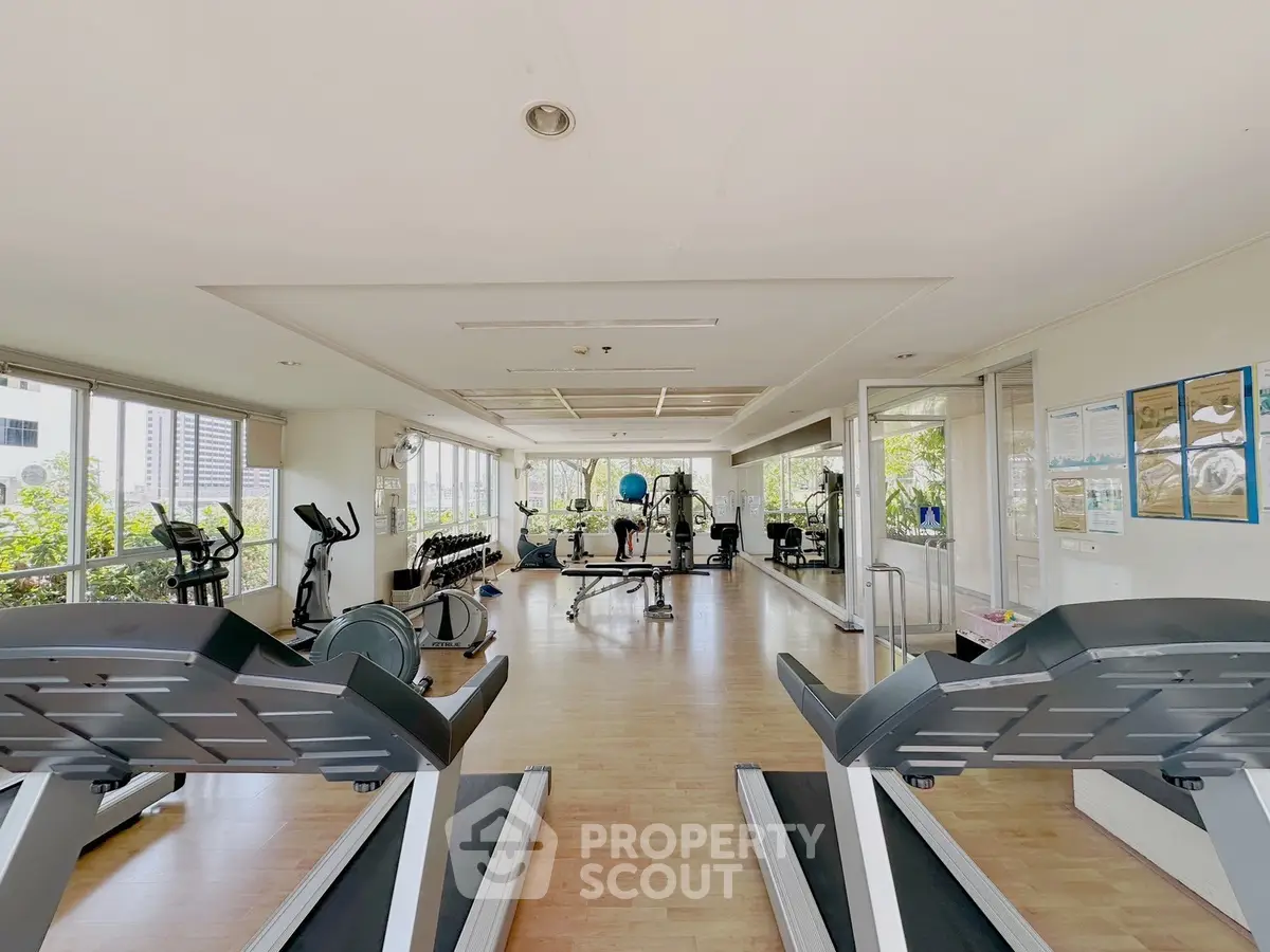 Spacious gym with modern equipment and large windows offering a bright and airy workout environment.