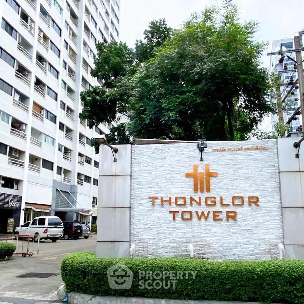 Thonglor Tower entrance with modern signage and lush greenery, showcasing urban living in a high-rise building.