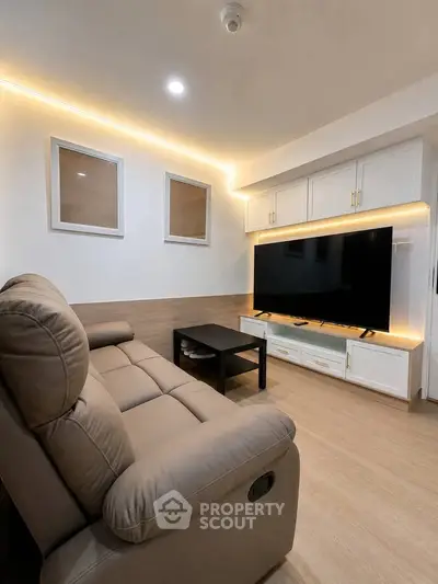 Modern living room with cozy sofa and large TV, featuring ambient lighting and sleek cabinetry.