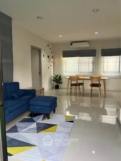 Modern living room with stylish blue sofa and dining area, featuring sleek tiled flooring and natural light.