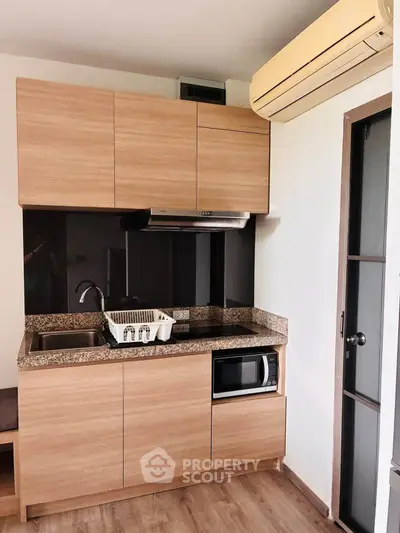Modern compact kitchen with wooden cabinets, granite countertop, and built-in microwave in a cozy apartment.