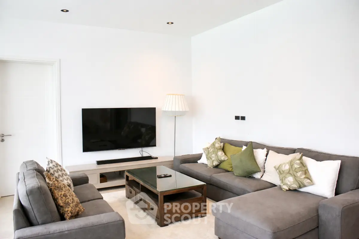 Modern living room with stylish gray sofas, wall-mounted TV, and elegant decor in a cozy setting.