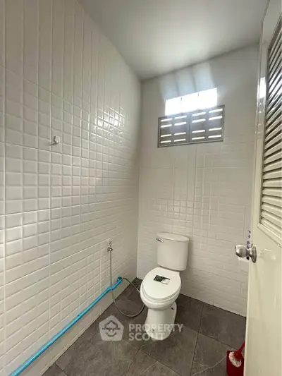 Modern bathroom with tiled walls and floor, featuring a toilet and natural light from a small window.