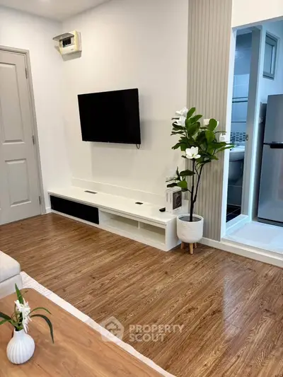 Modern living room with wooden flooring and wall-mounted TV, adjacent to a sleek kitchen area.
