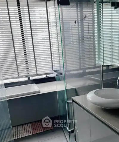 Modern bathroom with glass shower and large window in urban apartment.