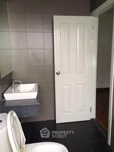 Modern bathroom with sleek sink and tiled walls, featuring a white door and toilet.