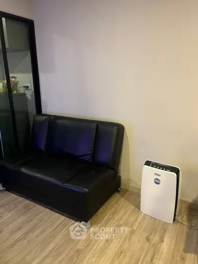 Modern living room with sleek black sofa and air purifier on wooden floor.