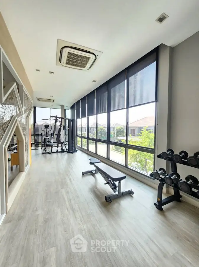 Modern gym with large windows and fitness equipment in a bright, spacious room.