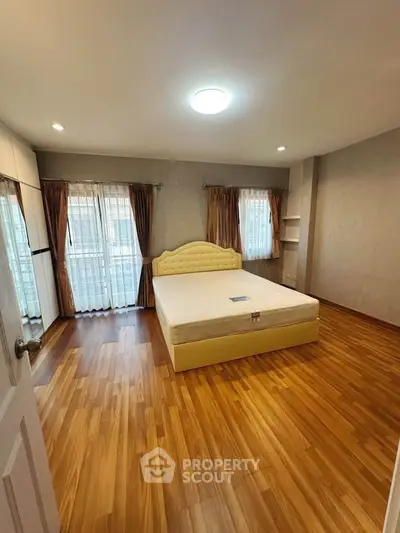 Spacious bedroom with wooden flooring and large windows for natural light.