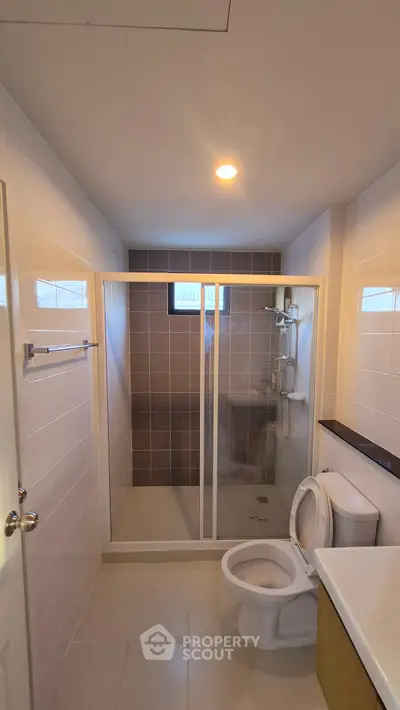Modern bathroom with shower and toilet, featuring sleek tiles and bright lighting.
