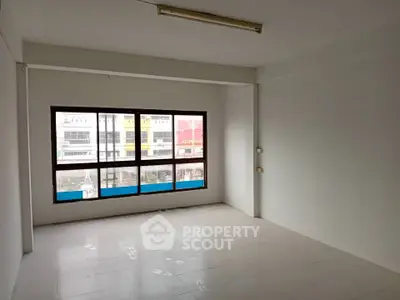 Spacious unfurnished room with large window and natural light in modern building.