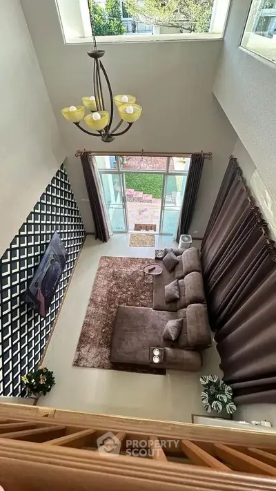 Spacious living room with high ceiling and modern decor, featuring large windows and elegant lighting.