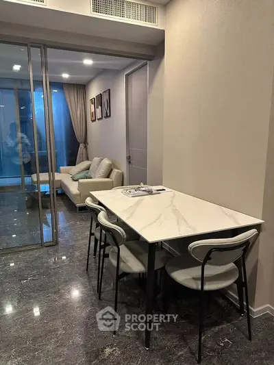 Modern dining area with marble table and elegant chairs, leading to a cozy living room with a sofa and artwork.