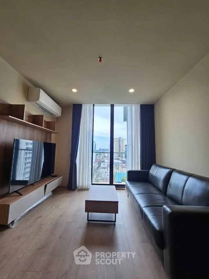 Modern living room with large window offering city view, sleek furniture, and wooden flooring.