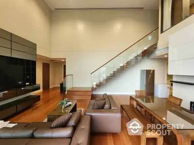 Spacious living room with high ceilings, modern furniture, and a floating staircase leading to an upper level, bathed in natural light.